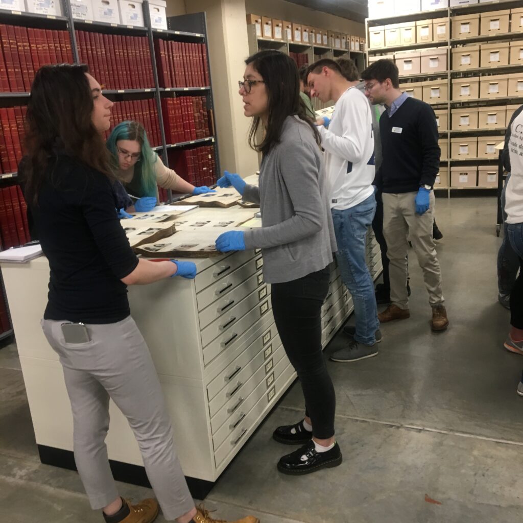 Students standing in an archive facility, wearing gloves and working with historic documents.